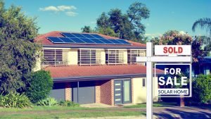 A picture of a modern California home with solar panels on top and a for sale sign out front that says "Solar Home"