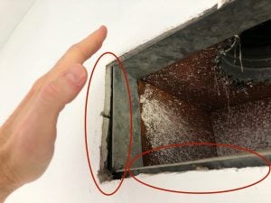 A picture of a hand being placed up to an open air vent in a house with gaps between the drywall and the air vent, letting hot attic hot air leaking into the house.