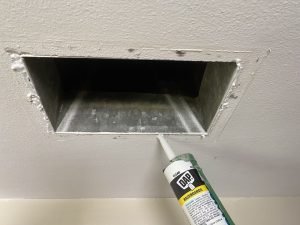 An air duct with the cover off, and caulking around the outside of it. This helps prevent hot attic air from getting into the room.