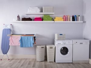 Photo of a bright laundry room with a washer, dryer, ironing board, drying rack and colorful towels and bottles.