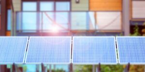 A picture of solar panels lined up with a modern house blurred out in the background, indicating net-zero energy buildings.