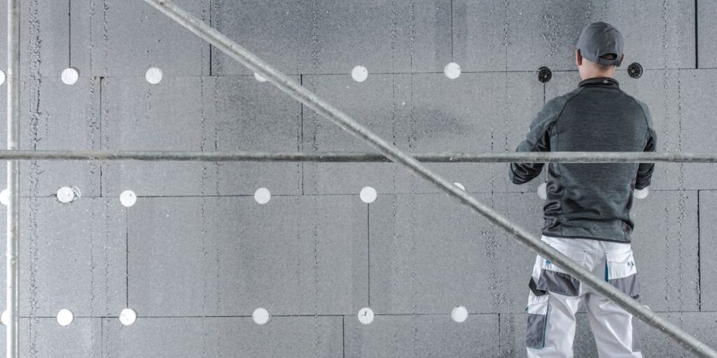 a man on scaffolding installing grey wall insulation on a wall