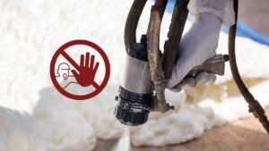 A picture of a spray foam gun spraying insulation downward, with a caution sign just to the left of it.