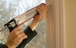 A homeowner caulking around window gaps in the drywall.