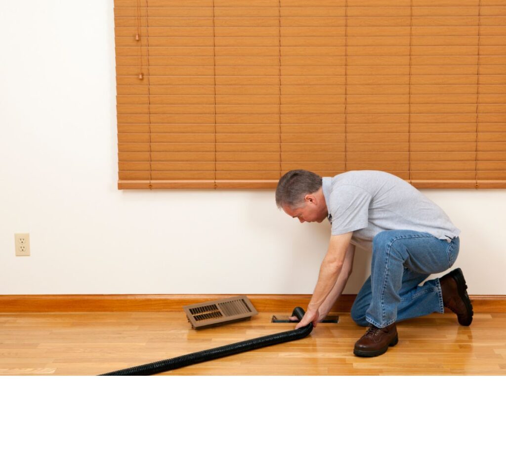 A man cleaning the exterior of a floor air duct vent in a home