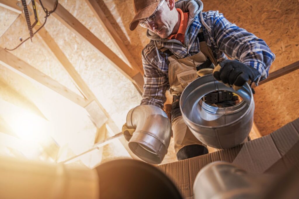 A technician replaces parts of an HRV system in an attic