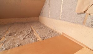 A closeup of cellulose insulation applied in a wall and flooring of an attic