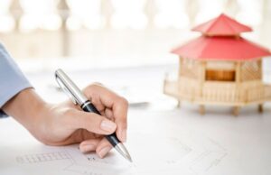 A homeowner drawns out a blueprint on a countertop with a modular home model also atop the paper in the background