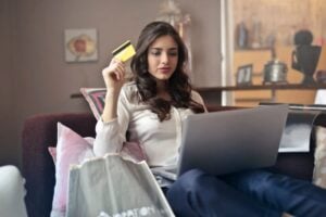 A homeowner sitting on the couch with credit card in hand searches for heat recovery ventilators on her laptop