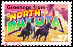 A vintage, full color stamp with an image of wild horses and text that reads "Greetings from North Dakota."