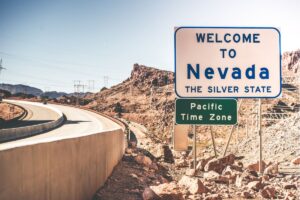 A roadsign at the stateline in the foreground welcomes vistors to Nevada with mountainous peaks in the background