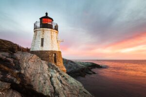 A lighthouse along the rocky Rhode Island coastline during sunset