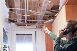 A homeowner on her cellphone points to the ceiling where radiant barriers are to be installed, suggesting some sort of installation issue