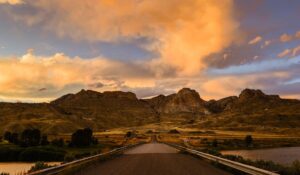 A horizontal shot of a Wyoming highway approaching the mountains with clouds and a breathtaking sunset above