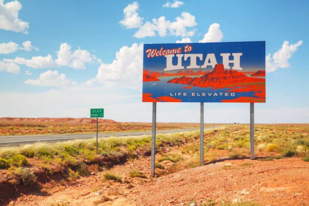 A shot of the 'Welcome to Utah' road sign at the state line, with desert, blue sky and clouds in the background
