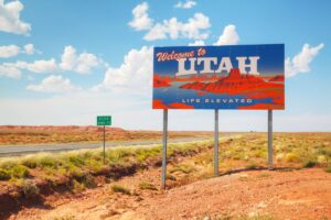 A shot of the 'Welcome to Utah' road sign at the state line, with desert, blue sky and clouds in the background