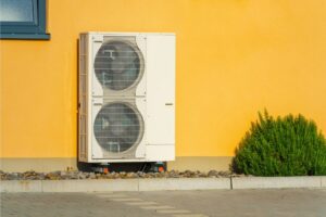 A ductless heat pump unit up against a wall outside a home