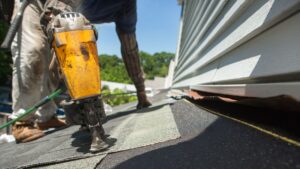 A carpenter nails light grey shingles to a roof