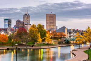 The downtown Indianapolis riverfront at dusk in the fall with skyscrapers poking out behind the green space