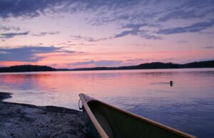 The tip of a canoe on the edge of a lake in the Northwoods of Minnesota at sunset