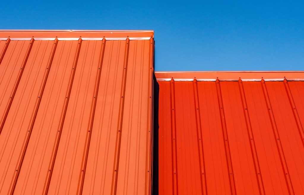 Closeup of two uneven metal roof sections on a home, one red the other orange