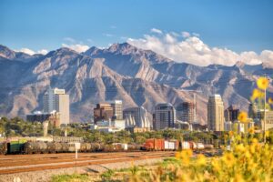 A view of Salt Lake City, Utah with green space and rail lines in the foreground and mountain peaks in back