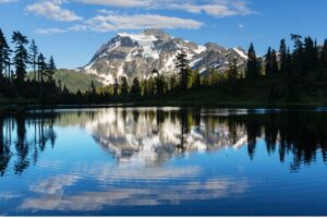 A lake in the foreground reflects blue sky Washington's Mount Rainer in back