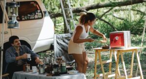 A couple uses a solar oven to cook food outside their van at their campsite