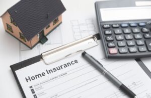 A home insurance form on top of a table next to a calculator and model home