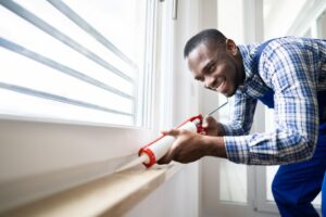 A homeowner applies window caulk to the bottom sill on a window's interior.