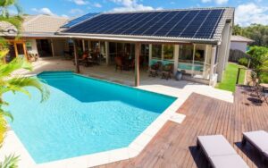 a backyard pool with light blue water and pool heating solar panels on the back of the home roof