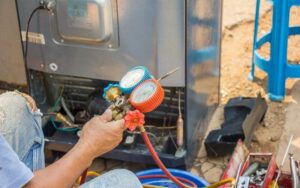 a man holding up a refrigerant pressure meter device attached to an air conditioning unit