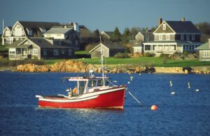A fishing boat on the water in front of several green homes along the Rhode Island coastline.