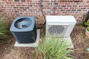 The condesner unit of a ductless mini-split next to an air conditioner outside a home