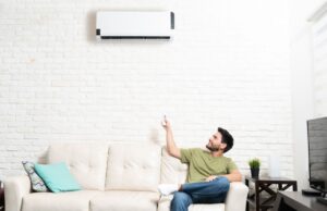 A homeowner on a couch adjusts the setting of his mini-split using a remote control