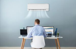 A homeowner sits at a desk against a wall below a mini-split's head unit near the ceiling