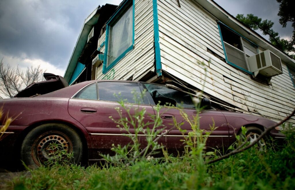 A house without hurricane ties displaced by a storm sits atop a compacted car