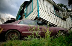 A house without hurricane ties displaced by a storm sits atop a compacted car