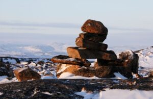 A rock formation atop a plateau in Nunavut, Canada, with rolling, snow-capped hills off in the distance