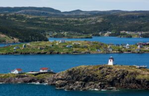 The coastline along St. John's Bay, Newfoundland, with rolling hills, scattered houses, and a lighthouse front and center