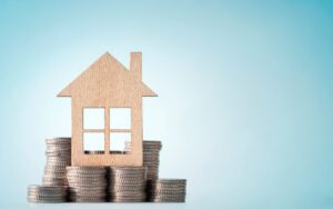 A wood cutout modular home frame sitting atop stacks of quarters