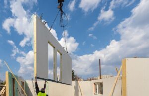 A module of a modular home being lowered by a crane with a worker grasping it as it comes down