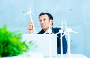 A homeowner on his laptop at a desk, holding and a model small wind turbine and pondering it