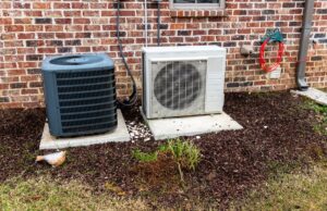 The compressor unit of a mini-split next to a central AC unit outside a home