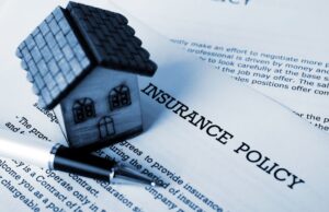Closeup on a home insurance policy on a table with a model home and pen atop the paper