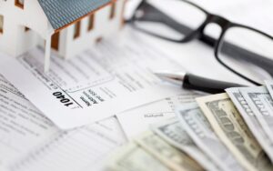 Closeup on various tax documents, rebate forms, a stack of cash and a model home on a tabletop