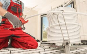 A technician kneeling on the floor cuts a piece of cable from a spool during a radiant floor heating system installation