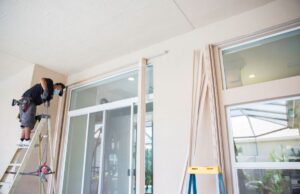 A homeowner on a ladder installing hurricane window panes above an interior door in his home