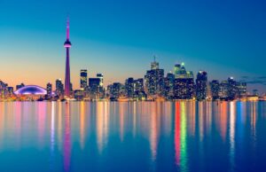 The waterfront in downtown Toronto at dusk, with the skyline in back and lights shimmering off Lake Ontario
