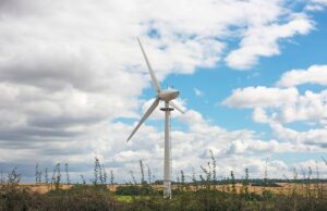 A small wind turbine in a field with clouds and blue sky in the background